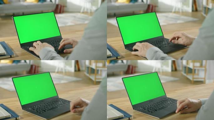 专业的自由职业者坐在他舒适的客厅的桌子旁，在带有绿色模拟屏幕的笔记本电脑上工作。