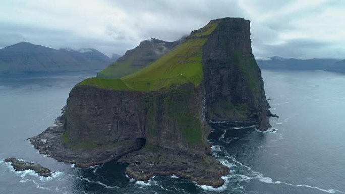 空中: 在绿草如茵的小岛上飞行，黑色的岩石悬崖高耸在海上。