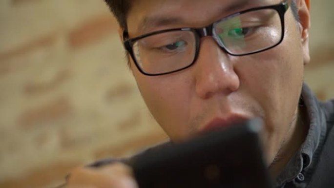 早上吃早餐时用智能手机的亚洲男子的4K CU脸