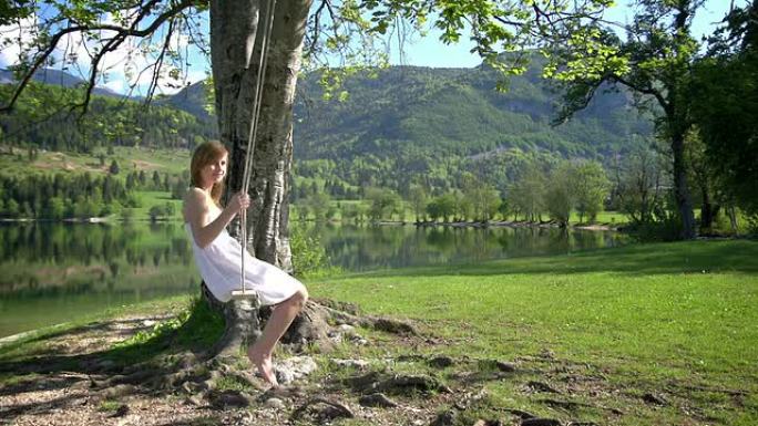 一个穿着白色连衣裙的女孩在湖边荡绳子