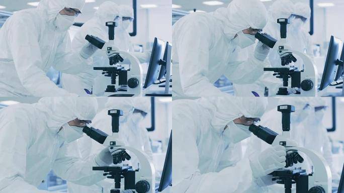 在实验室中，穿着防护服的科学家进行研究，使用显微镜并将数据输入个人计算机。生产半导体和药品的现代工厂