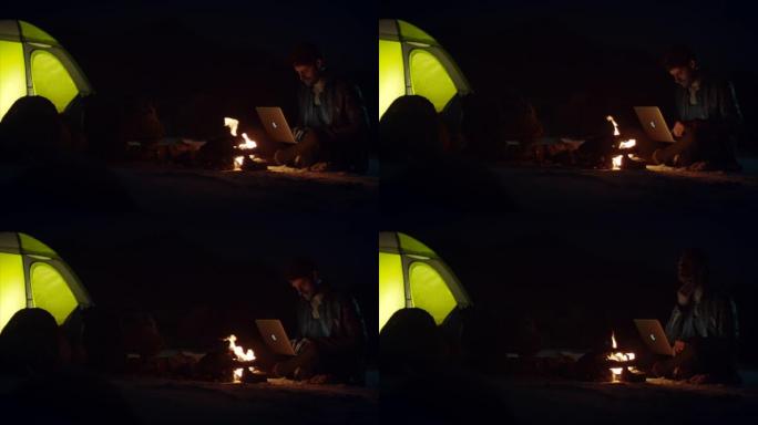 男人拿着笔记本电脑坐在篝火旁