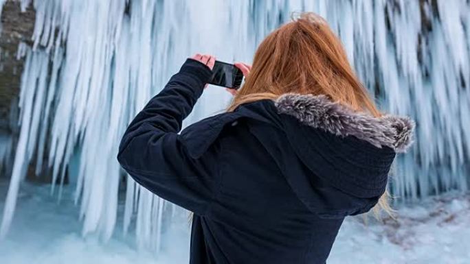 年轻女子在冬天为瀑布拍照