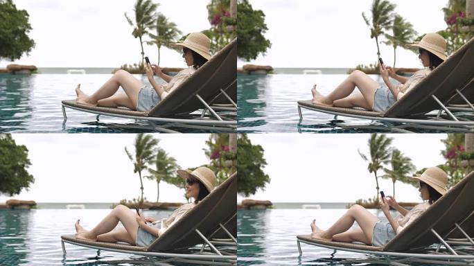 轻松的亚洲年轻女子在度假游泳池里看手机