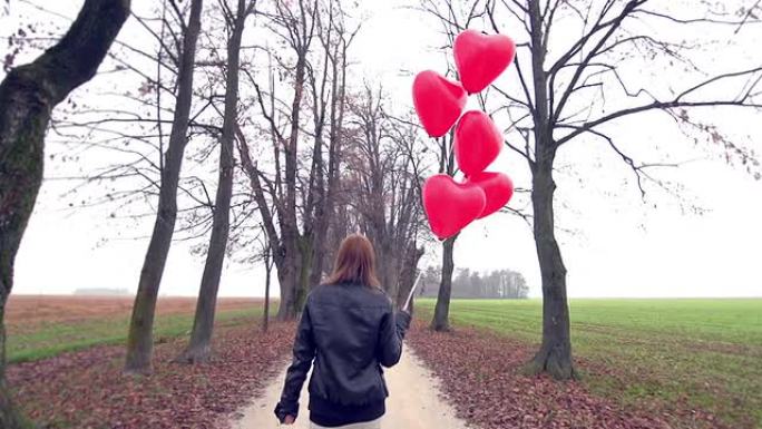 女孩带着红色心形气球在公园里散步