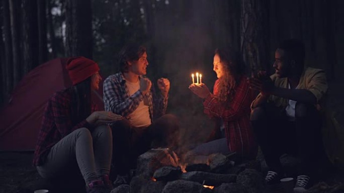 富有创造力的人在森林里祝贺他们的朋友生日，拍手并给她蛋糕，而女孩正在吹蜡烛和微笑。自然和庆祝概念。