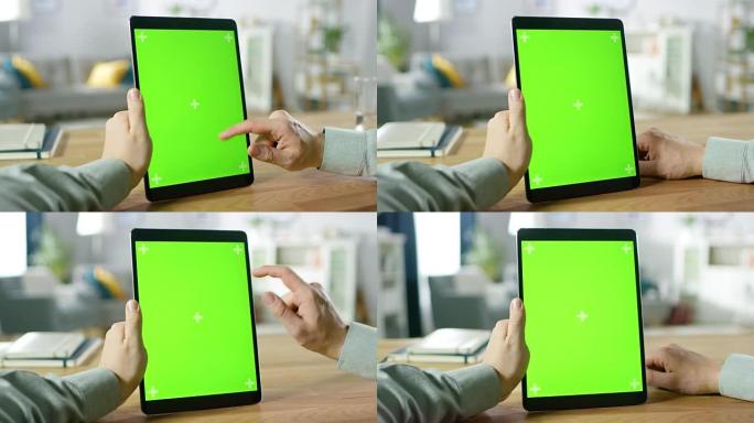 坐在办公桌前，在肖像模式下的绿色模拟屏幕数字平板电脑上使用手势的人的特写镜头。背景舒适的客厅。
