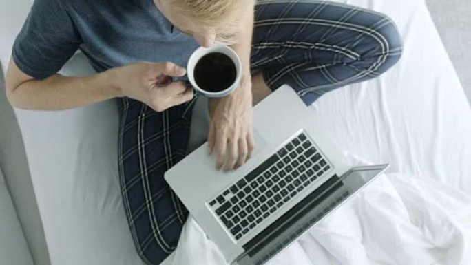穿着睡衣的男人喝咖啡和使用笔记本电脑