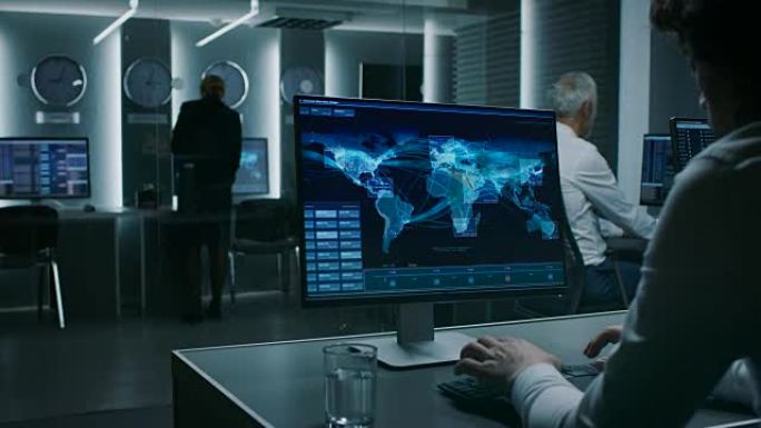 在系统控制室工作的网络安全主任在个人电脑上显示交通数据流的背影，房间里挤满了特别情报人员。