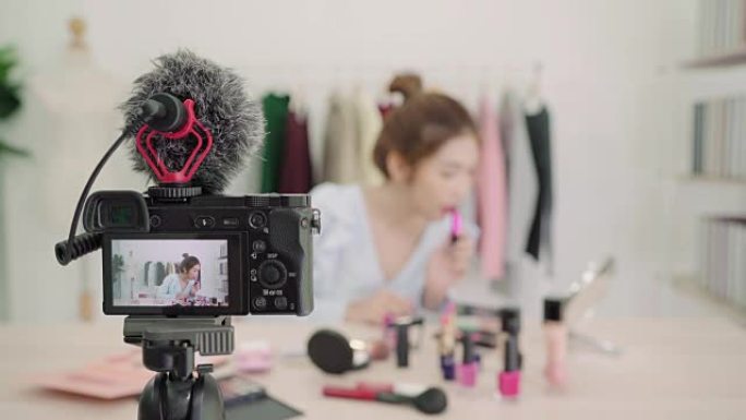 美容博主呈现美容化妆品坐在前置摄像头录制视频。美丽的亚洲女人在复习时使用刷子化妆教程通过互联网向社交