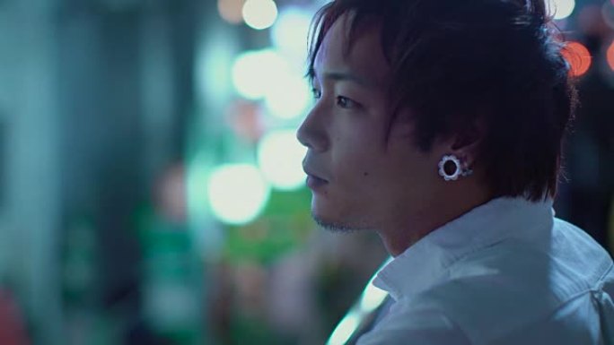 英俊的日本另类男人的肖像。在后台，大城市的广告广告牌灯光在夜晚发光。