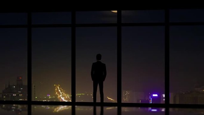 站在夜城背景全景窗户附近的男性