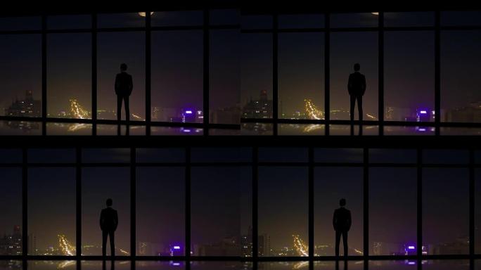 站在夜城背景全景窗户附近的男性
