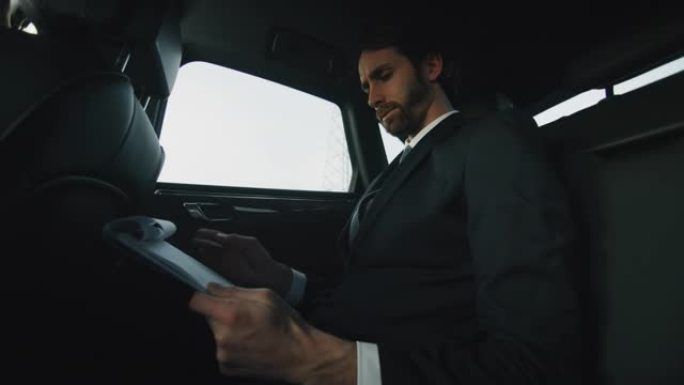 慢动作英俊的商人使用他的笔记本电脑在一辆现代汽车旅行期间与一个司机在市中心的白天