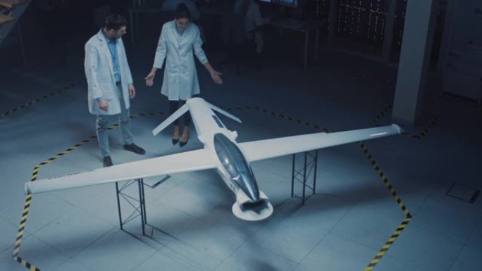 两名航空航天工程师在无人飞行器/无人机原型上工作。穿着白大褂说话的航空科学家，使用平板电脑。带有监视