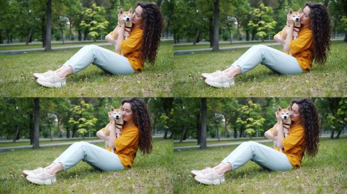 漂亮的年轻女子亲吻狗的枪口，微笑着坐在公园的草地上