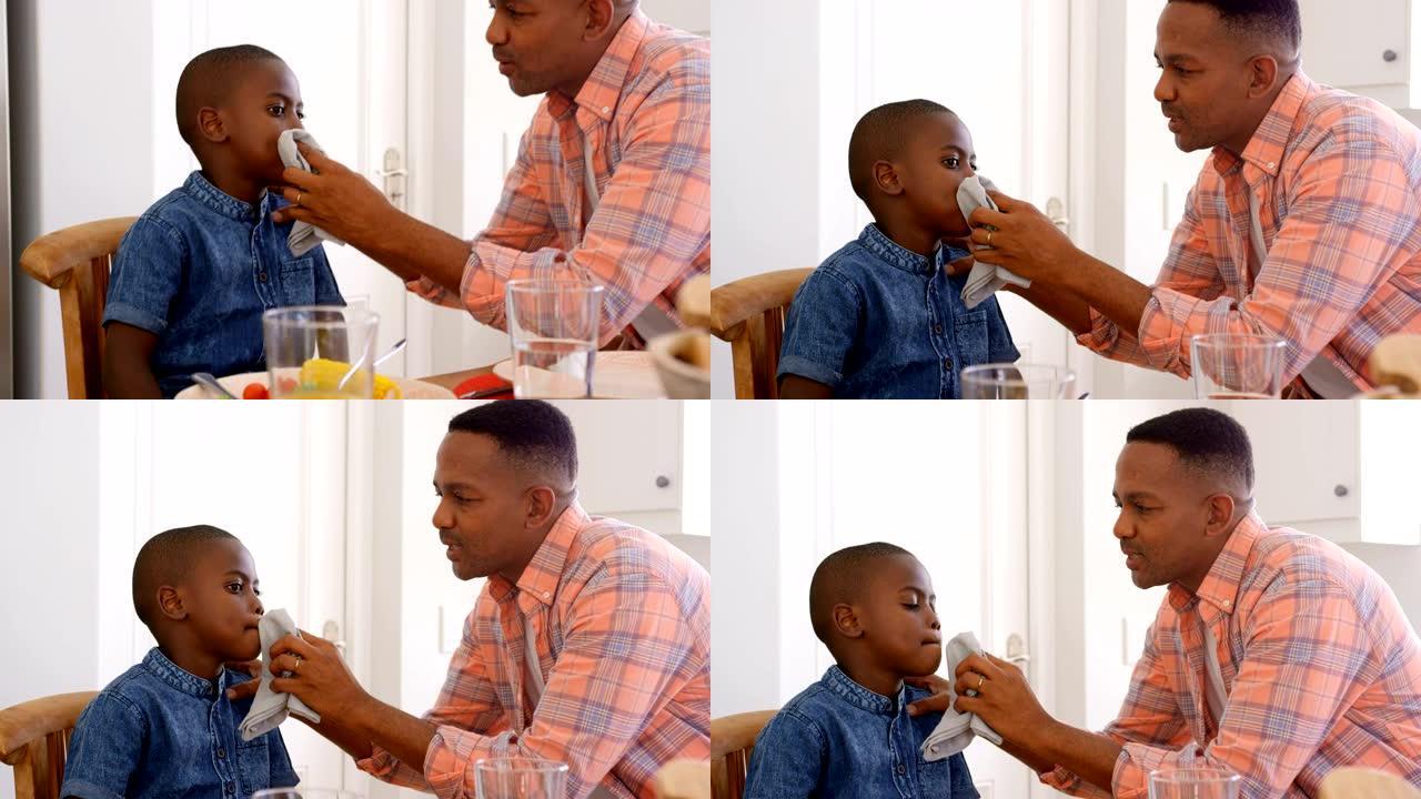 在舒适的家庭4k中，成年黑人父亲在餐桌上擦儿子的嘴的侧视图