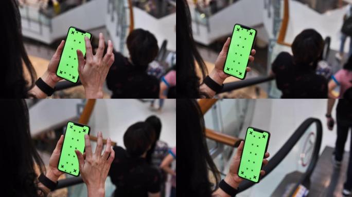 年轻女子在购物中心使用带绿屏自动扶梯的智能手机