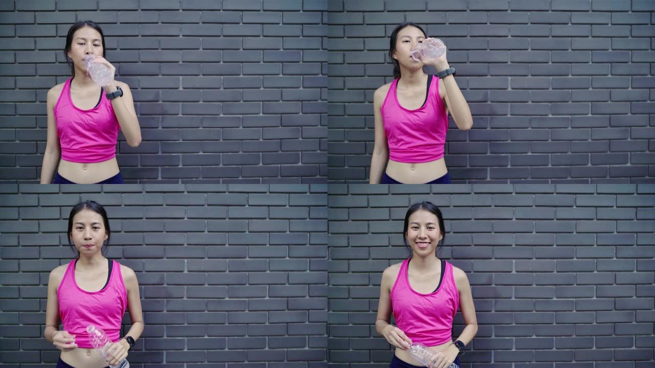 健康美丽的年轻亚洲跑步者妇女喝水，因为在城市的街道上跑步后感到疲倦。生活方式适合和积极的女性在城市概