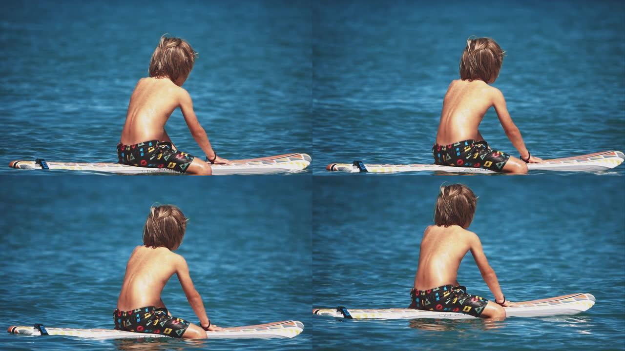 男孩坐在漂浮在海洋中的冲浪板上