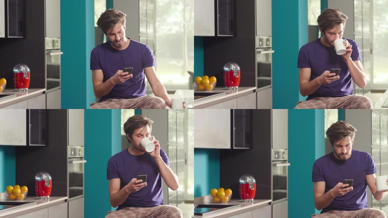 一个男人在厨房里吃早餐，在杯子里喝茶或牛奶时，用电话发送消息或打电话，并微笑。