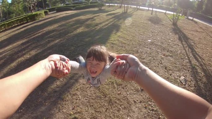 父亲在公园里旋转他的小女儿，孩子对着镜头微笑的视点镜头