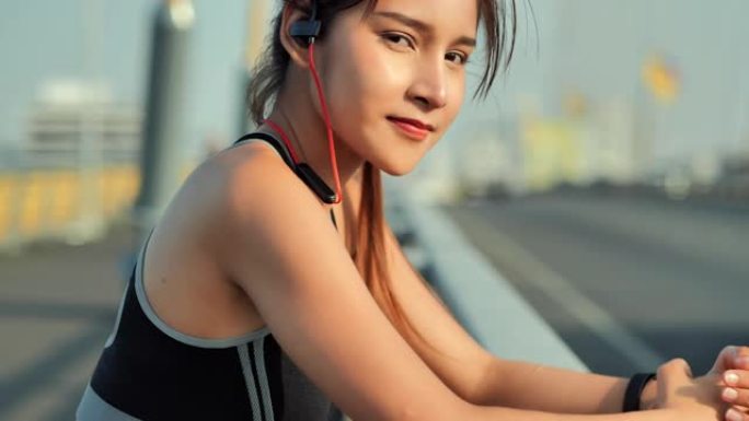肖像亚洲年轻女性微笑着对着相机，在城市的耳机上听音乐。生活方式，成功，力量，力量，健康，技术，力量，