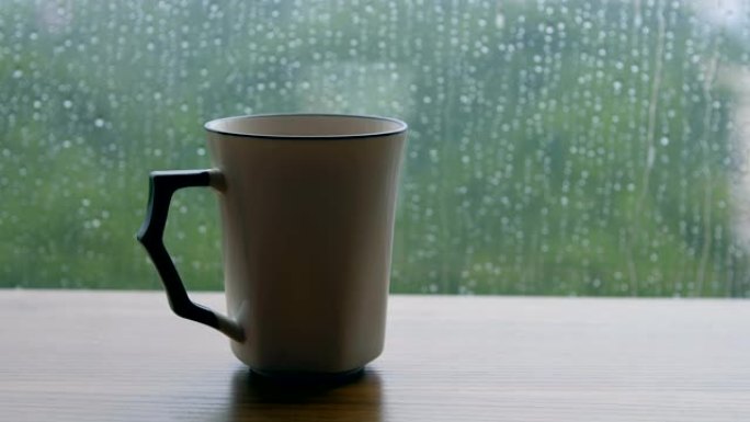 木制桌子上的咖啡杯，带有雨滴背景
