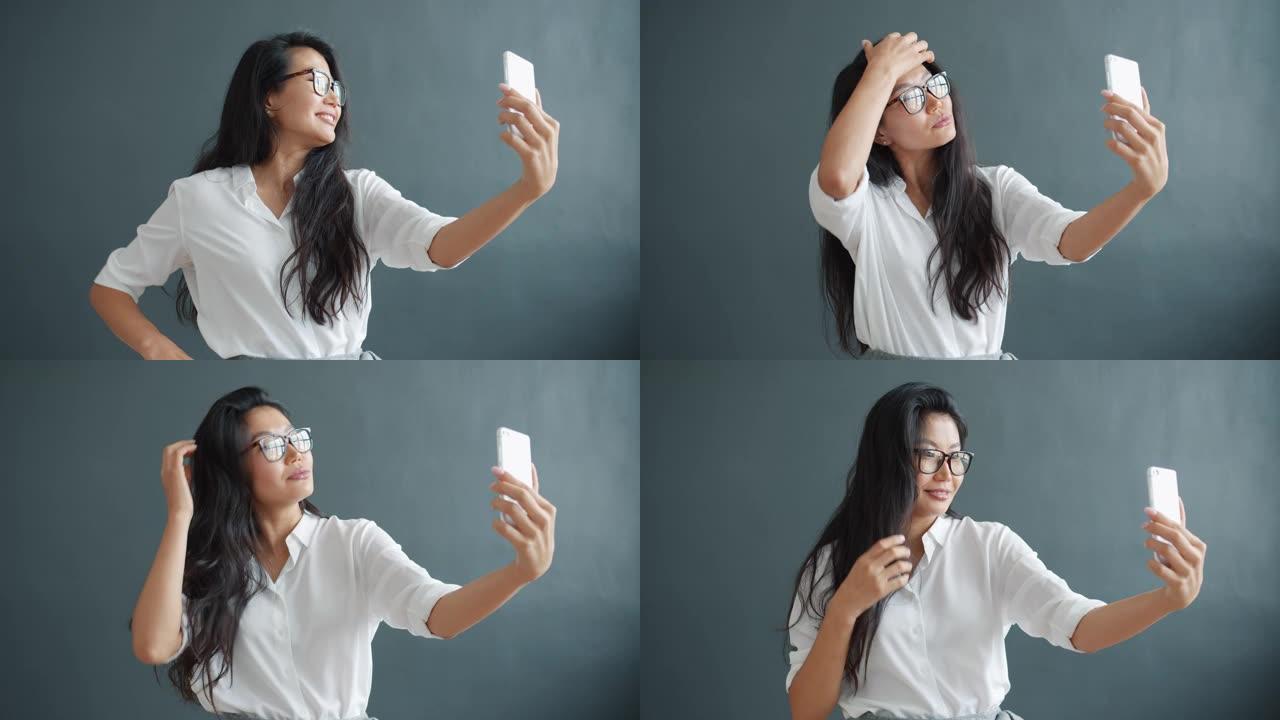 快乐的亚洲女孩在黑色背景下用智能手机相机自拍的肖像