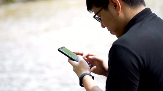 肩射-亚洲男子在典型的河流放松玩电话