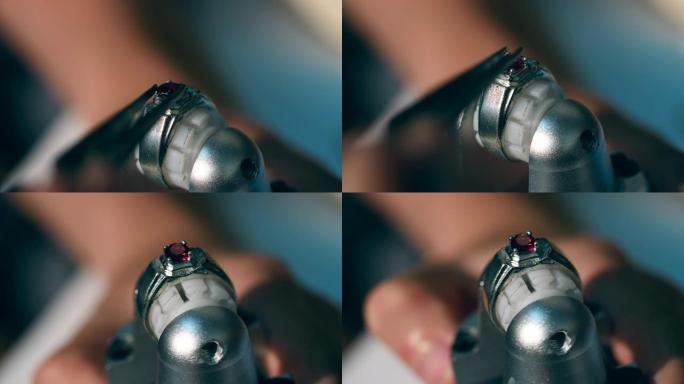 一个人在珠宝车间的戒指上放了一块红色宝石。