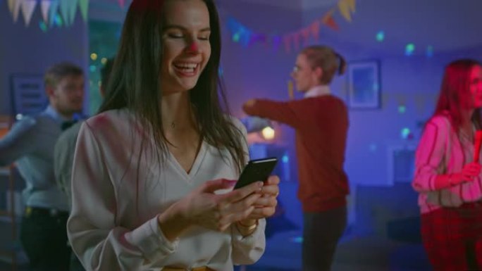 在野外聚会上: 美丽的年轻女孩使用智能手机，通过互联网和社交网络浏览。在背景人群中，年轻人跳舞，玩得
