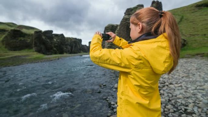 女人站在冰岛的Fjadrargljufur峡谷内，用智能手机拍照