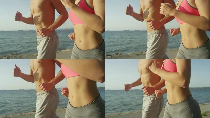 特写: 无法辨认的健康男人和女人，平坦的腹肌在海边慢跑。