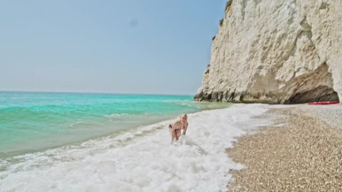 女士顽皮的年轻女子在意大利普利亚阳光明媚的绿松石海浪中嬉戏
