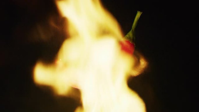 用叉子握住红辣椒的特写镜头，背景是火。