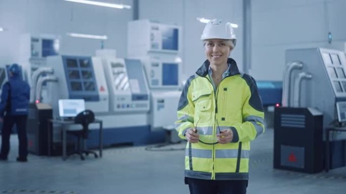 美丽的微笑女工程师穿着安全背心和安全帽。在现代制造工厂工作的职业女性。具有数控机械和机器人手臂的设施