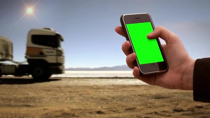 在荒芜之地的一条道路附近，男性手持智能手机绿屏。