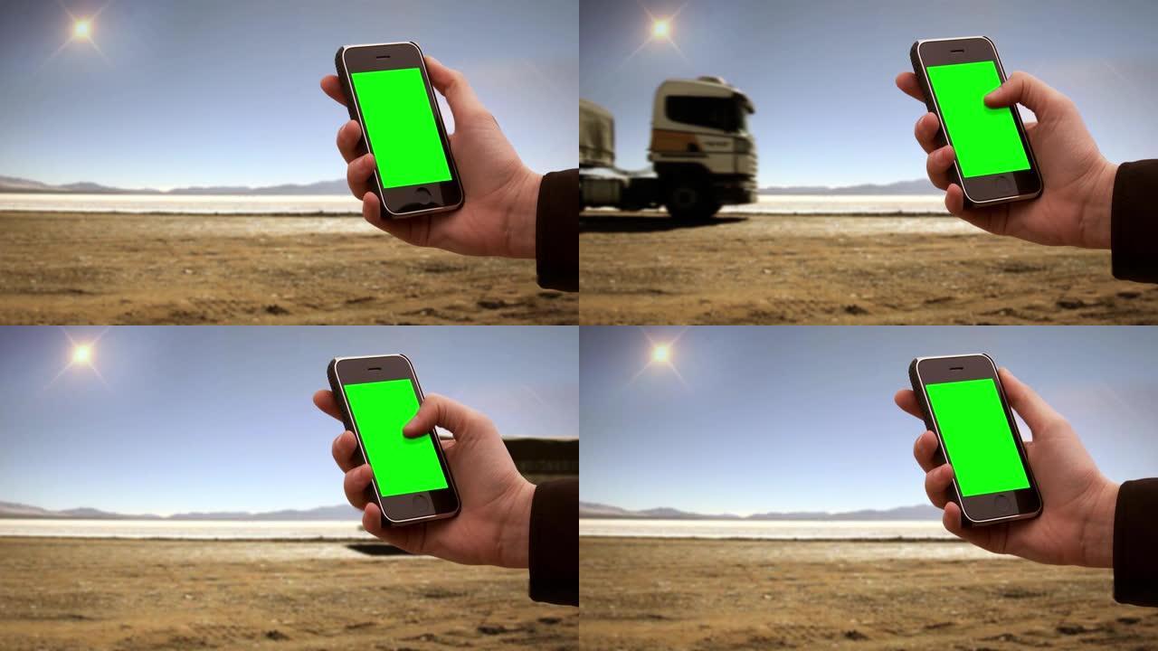 在荒芜之地的一条道路附近，男性手持智能手机绿屏。