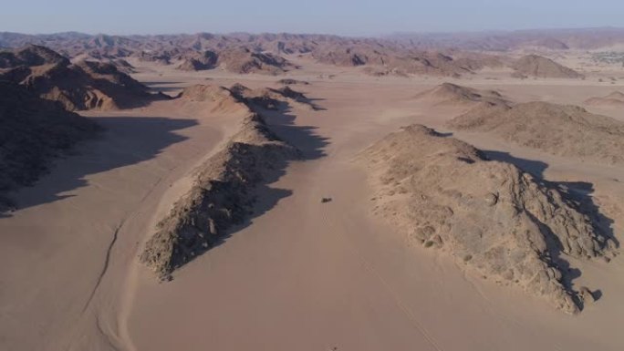 在纳米比亚纳米布沙漠的Hoanib山谷的山脉之间的沙道上行驶的4x4野生动物园车辆的4k鸟瞰图