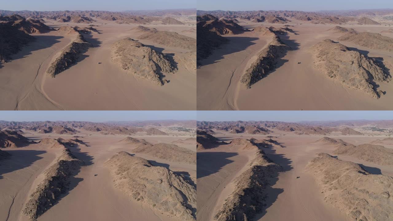在纳米比亚纳米布沙漠的Hoanib山谷的山脉之间的沙道上行驶的4x4野生动物园车辆的4k鸟瞰图