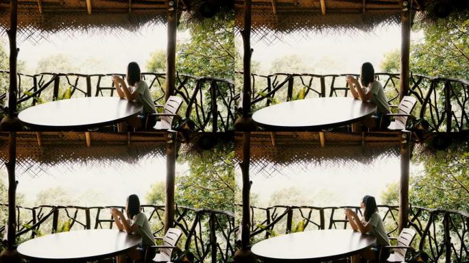年轻快乐的旅游女人在令人惊叹的热带森林酒店露台享受早晨咖啡的美丽背景照片。