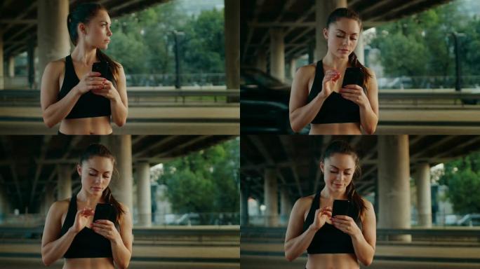 穿着黑色运动上衣的美丽强壮的健身女孩正在使用智能手机，在街上微笑。她在城市环境中，背景是汽车。