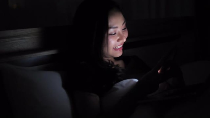 亚洲妇女晚上在床上使用智能手机