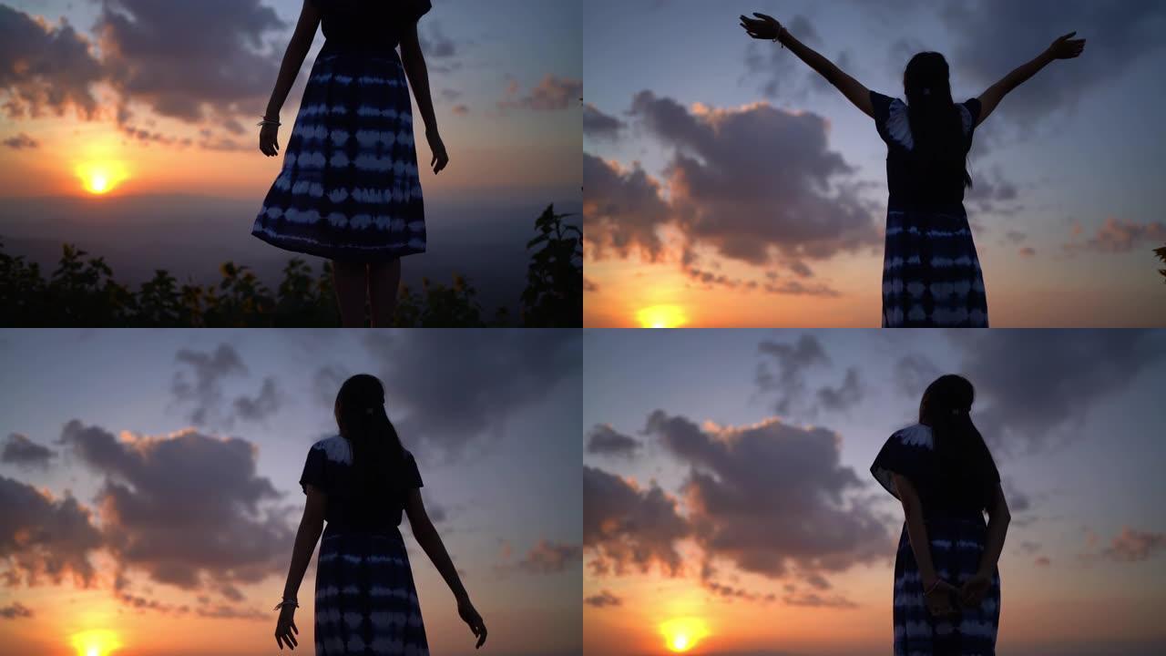 女人站在山上伸出手臂，看着日出或日落