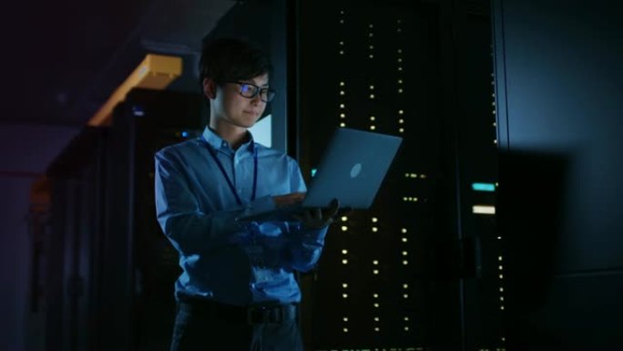 在黑暗的数据中心: 男性IT专家站在一排操作服务器机架旁边，使用笔记本电脑进行维护。云计算、人工智能
