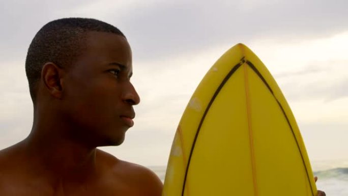 非裔美国男性冲浪者站在海滩4k冲浪板前视图