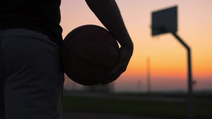 CU年轻人带着篮球在黄昏时走出室外篮球场