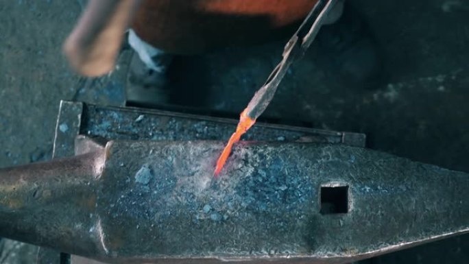 工作铁匠用铁锤敲打铁砧上的金属刀。