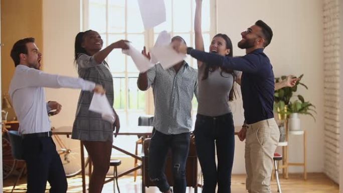 激动的多元化业务团队在办公室里扔纸跳舞